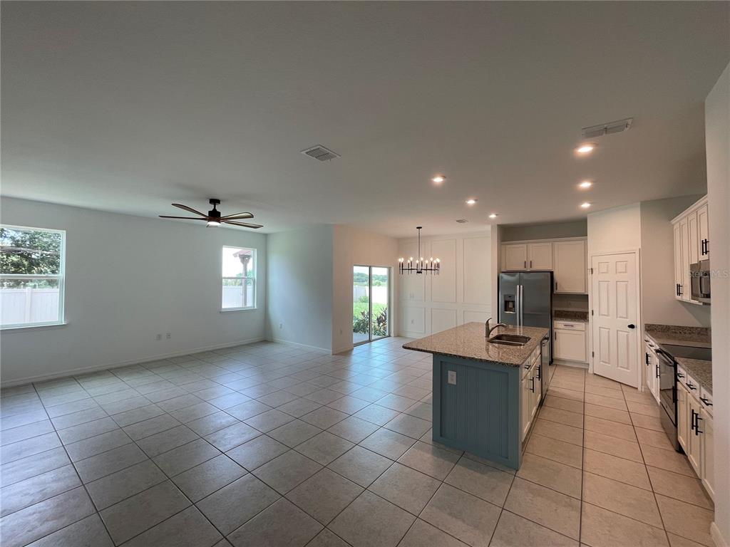 An open-concept kitchen and living area features tile flooring, a granite island, and white cabinetry — 689 CROWN ROSE DRIVE, EAGLE LAKE, FL