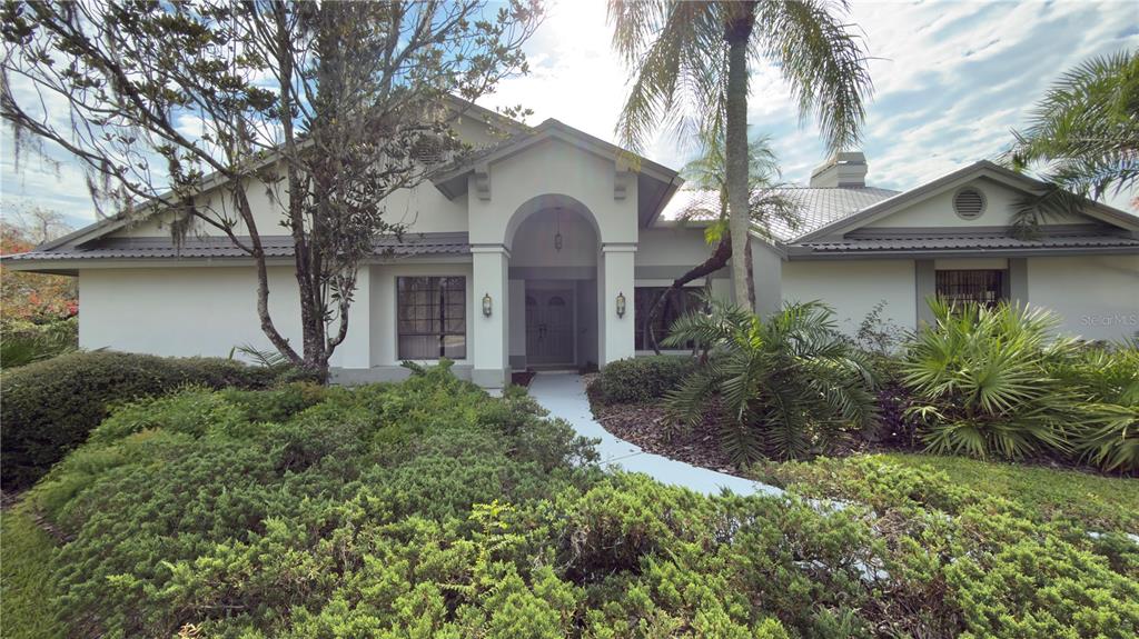 A single-story house with a covered entryway, metal roof, and extensive front yard landscaping — 5040 PINELAKE ROAD, WESLEY CHAPEL, FL