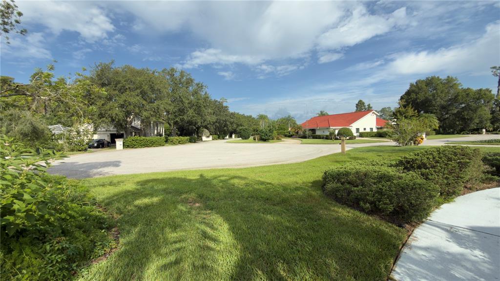 A paved cul-de-sac surrounded by green lawns, mature trees, and residential houses under a sky — 5040 PINELAKE ROAD, WESLEY CHAPEL, FL