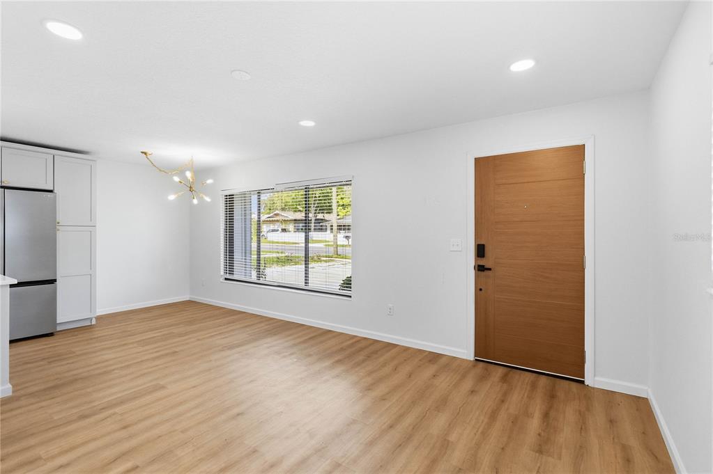 A bright room features light wood-look flooring, a modern chandelier, and a wooden front door — 2445 SANFORD AVENUE, SANFORD, FL