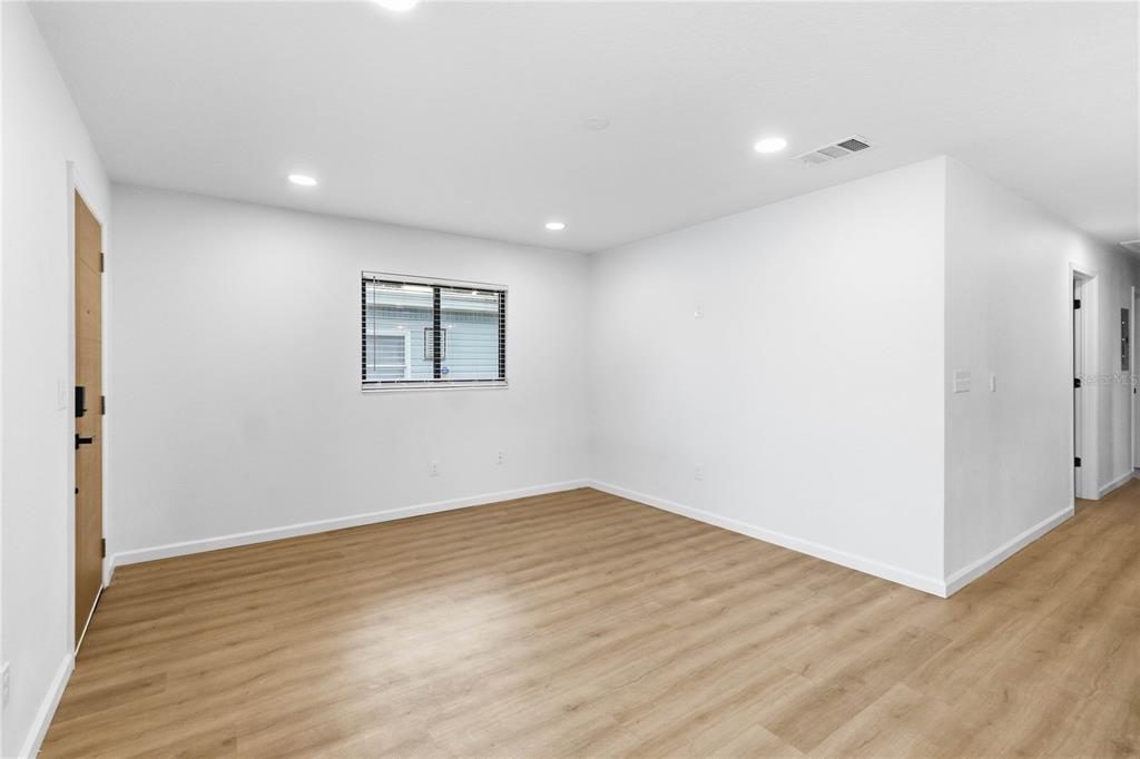 A bright, empty room features light wood-look flooring, white walls, recessed lighting, and two windows — 2445 SANFORD AVENUE, SANFORD, FL