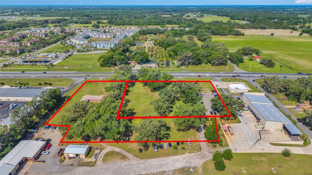 An aerial view shows a large, grassy, tree-filled lot outlined in red next to commercial buildings — 9935 N US HIGHWAY 301, WILDWOOD, FL