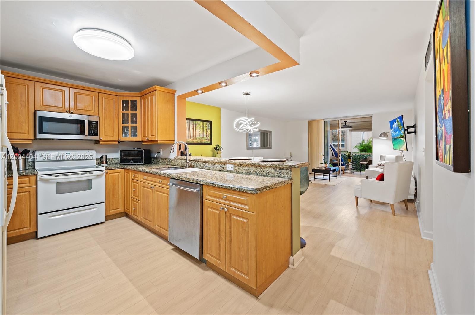 A kitchen with light wood cabinets and granite countertops opens into a bright living area — 424 SE 10th St # 104, Dania Beach FL 33004, DANIA BEACH, FL
