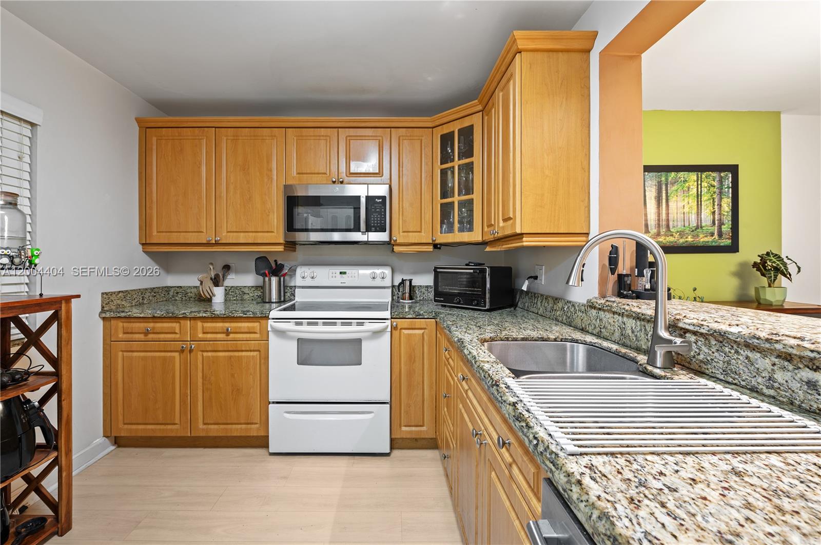 A kitchen features light wood cabinets, granite countertops, a white stove, and a stainless sink — 424 SE 10th St # 104, Dania Beach FL 33004, DANIA BEACH, FL