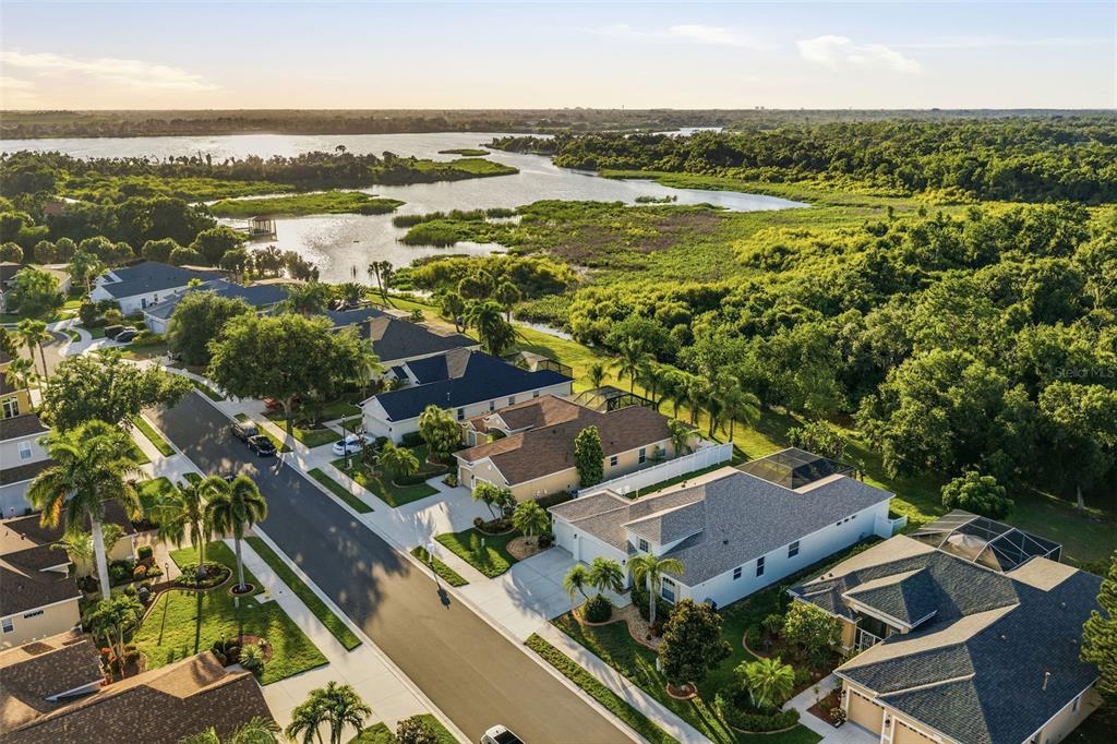 An aerial view shows a suburban neighborhood with houses bordering a large lake and forest — 6631 63RD TERRACE E, BRADENTON, FL