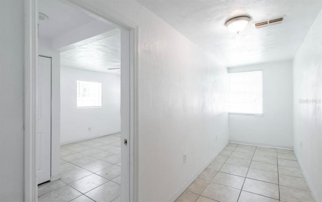 A bright room with white walls and light-colored tile flooring leads into an adjacent room — 416 S CAROLINE STREET, DAYTONA BEACH, FL