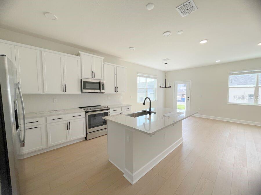 A modern kitchen features white cabinets, stainless steel appliances, and a central quartz-topped island — 15236 TRIBUTE OVATION WAY, WINTER GARDEN, FL