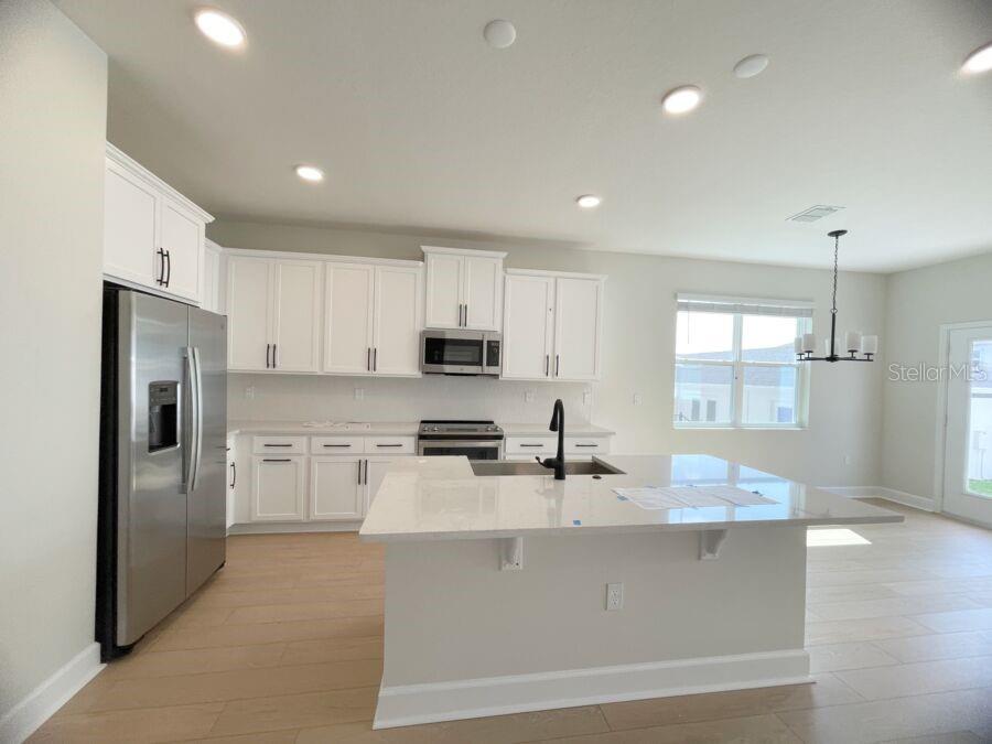 A modern kitchen features white cabinets, stainless steel appliances, and a large central island — 15236 TRIBUTE OVATION WAY, WINTER GARDEN, FL
