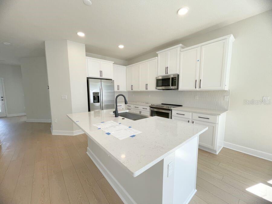 A modern kitchen features white cabinets, stainless steel appliances, and a large quartz-topped island — 15236 TRIBUTE OVATION WAY, WINTER GARDEN, FL