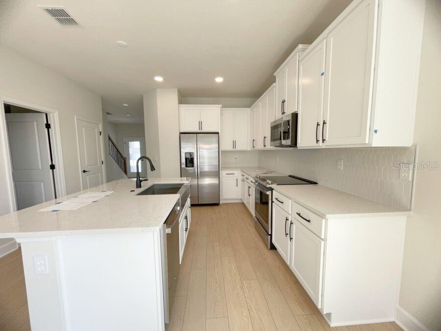 A modern kitchen features white cabinets, stainless steel appliances, and a large quartz-topped island — 15236 TRIBUTE OVATION WAY, WINTER GARDEN, FL