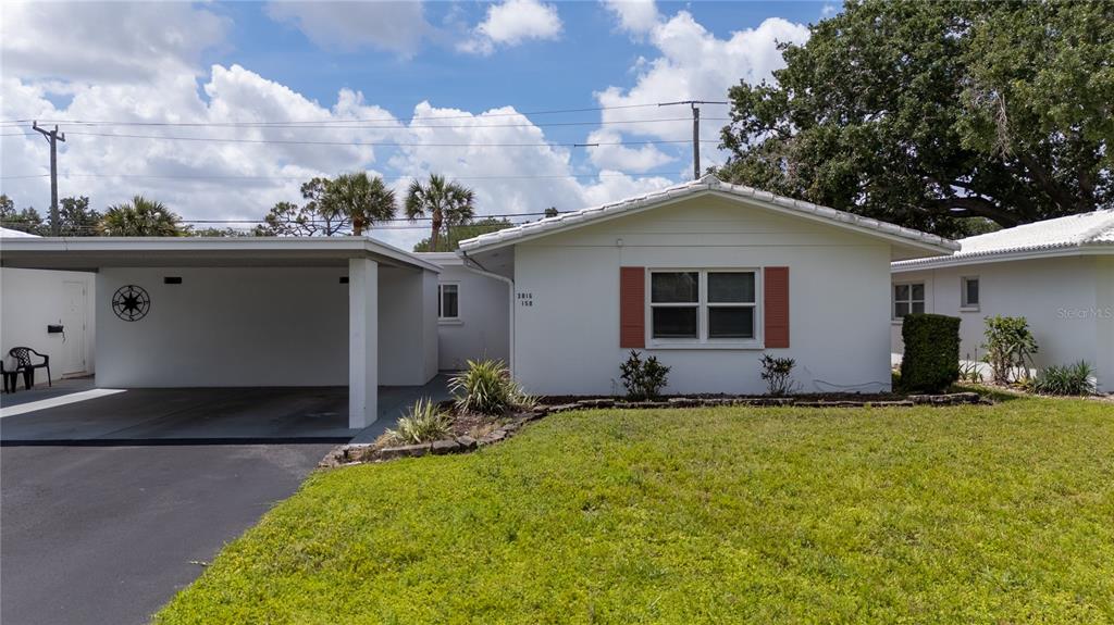 A white single-story house features a carport, a front lawn, and a window with shutters — 3816 ROXANE BLVD UNIT 158, SARASOTA, FL