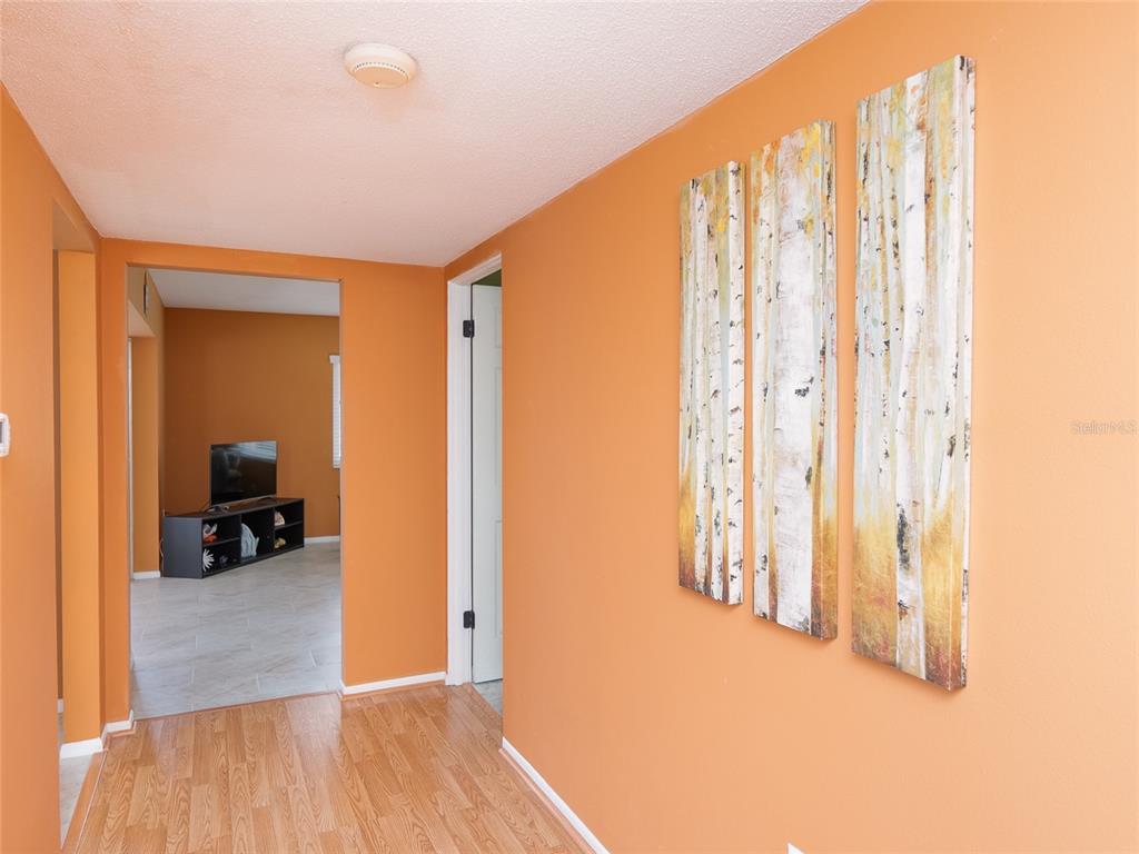 A hallway with orange walls, wood-look flooring, and a three-panel birch tree wall art piece — 3816 ROXANE BLVD UNIT 158, SARASOTA, FL