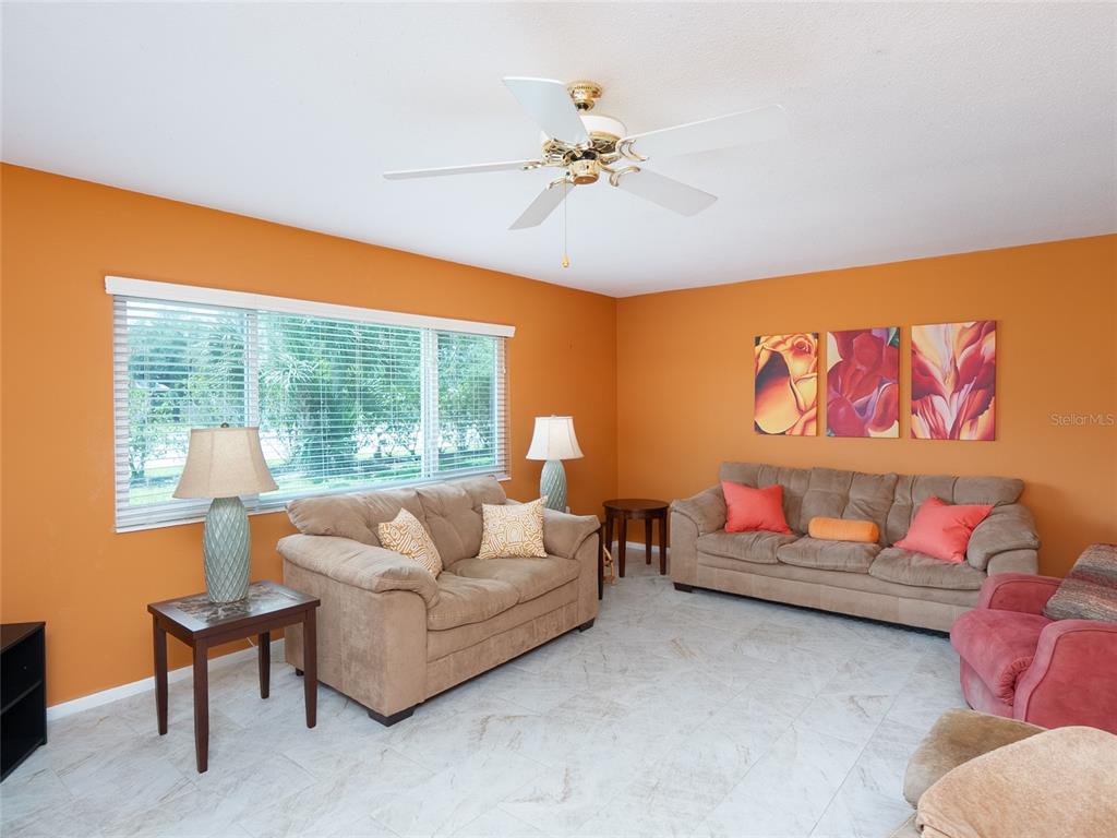 A living room features orange walls, two beige sofas, a ceiling fan, and tile flooring — 3816 ROXANE BLVD UNIT 158, SARASOTA, FL