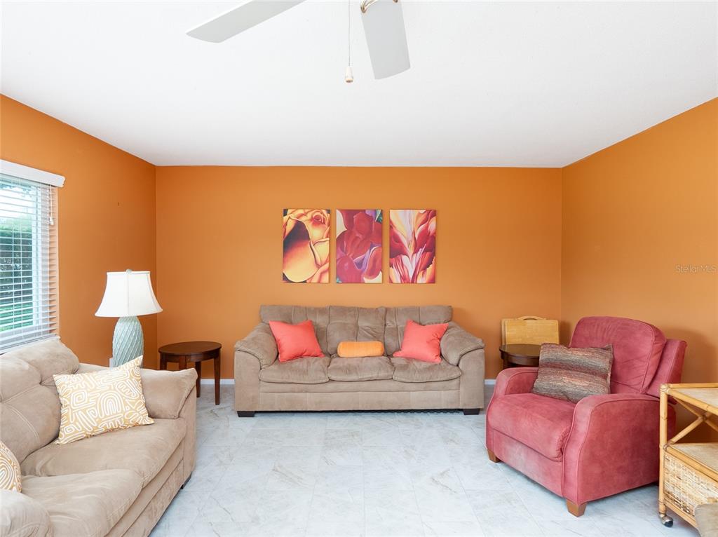 A living room features orange walls, a beige sofa, a red armchair, and tile flooring — 3816 ROXANE BLVD UNIT 158, SARASOTA, FL