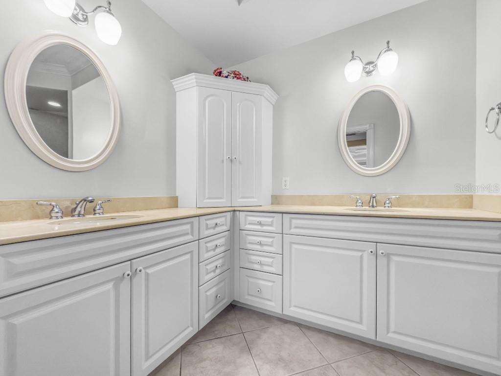 A bathroom features a double vanity with white cabinets, beige countertops, and two oval mirrors — 3314 WOOD THRUSH DRIVE UNIT 124, PUNTA GORDA, FL