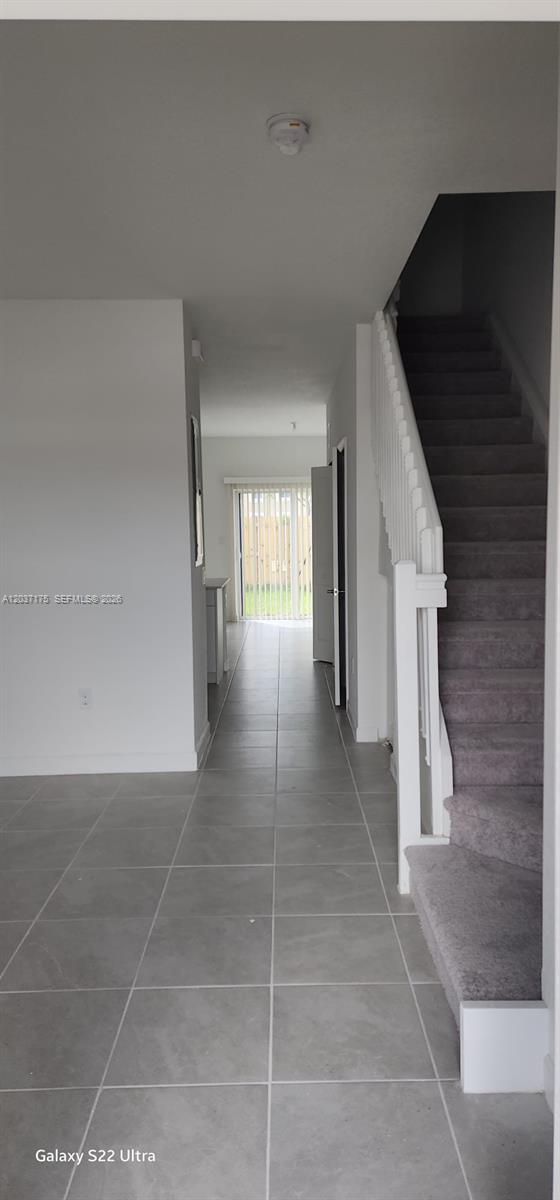 A hallway with gray tile flooring leads to a glass door, with stairs on the right — 12113 NW 23rd Court, Miami FL 33167, MIAMI, FL