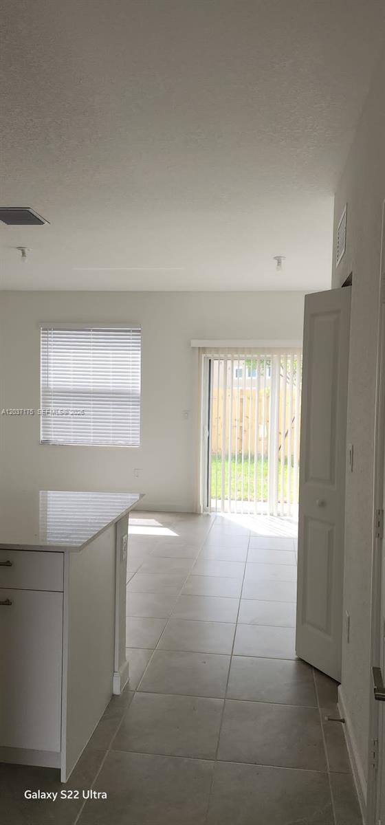 A kitchen island with a white countertop overlooks a tiled living area with sliding doors — 12113 NW 23rd Court, Miami FL 33167, MIAMI, FL