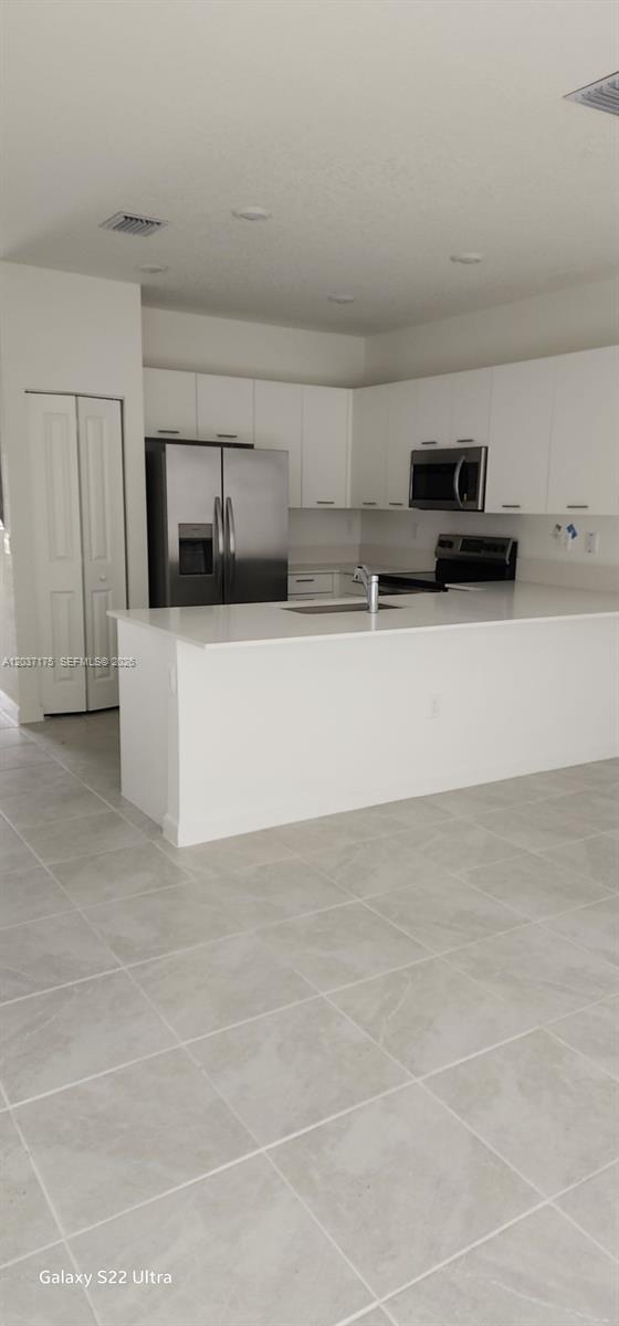 A modern kitchen features white cabinetry, stainless steel appliances, and a white quartz island — 12113 NW 23rd Court, Miami FL 33167, MIAMI, FL