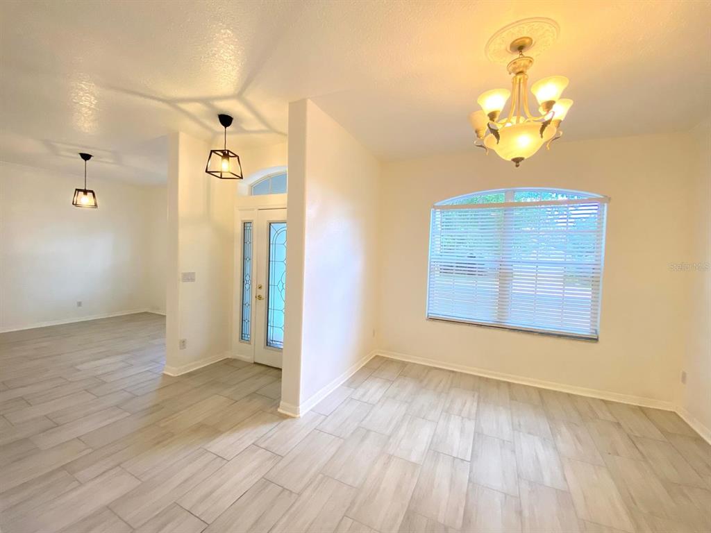 A bright entryway and dining area feature light wood-look tile flooring and a chandelier — 3837 FALLSCREST CIRCLE, CLERMONT, FL