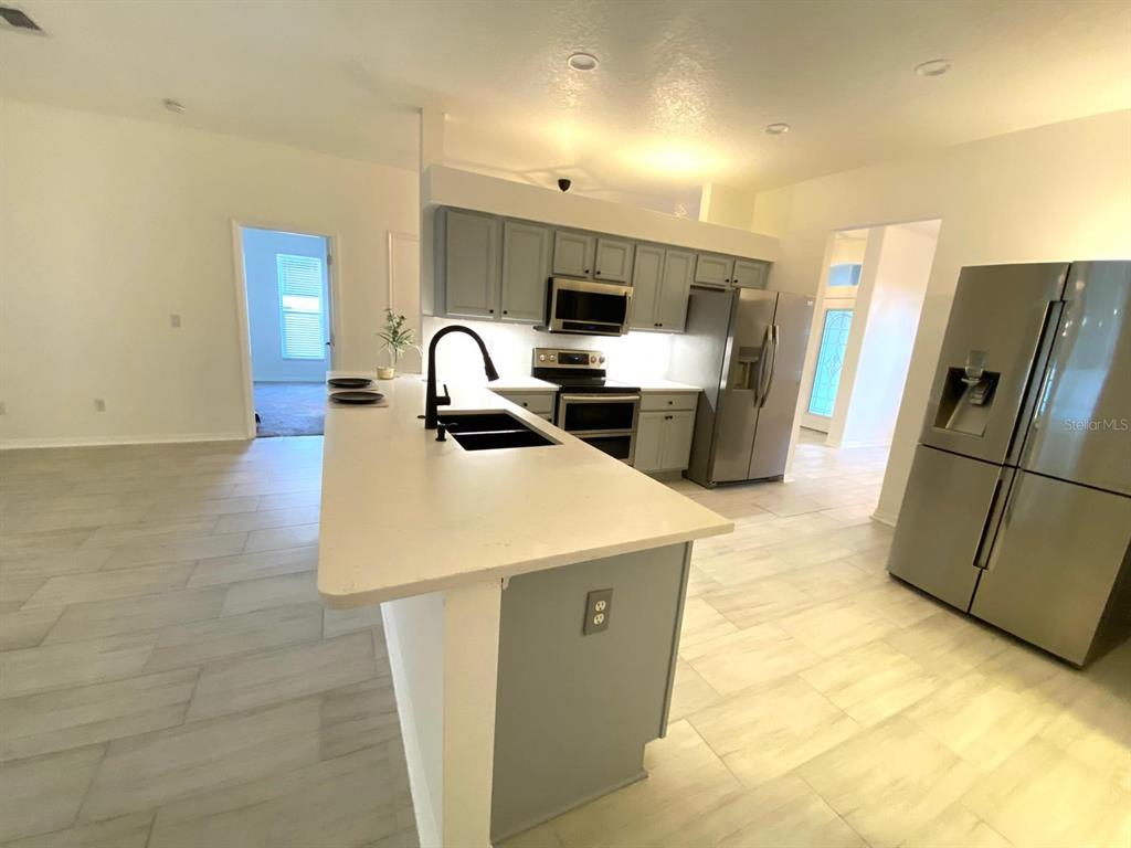 A kitchen features light gray cabinets, stainless steel appliances, and a white quartz island countertop — 3837 FALLSCREST CIRCLE, CLERMONT, FL