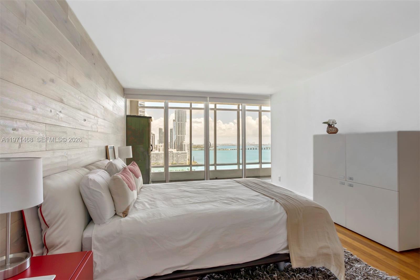 A bedroom features a light wood-paneled wall, a red nightstand, and floor-to-ceiling windows — 1717 N Bayshore Dr # 2740, Miami FL 33132, MIAMI, FL