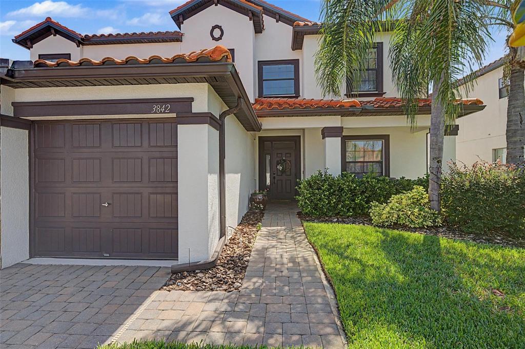 A two-story stucco house with a brown garage door, tile roof, and paved walkway — 3842 WELLINGBOROUGH COURT, LAND O LAKES, FL