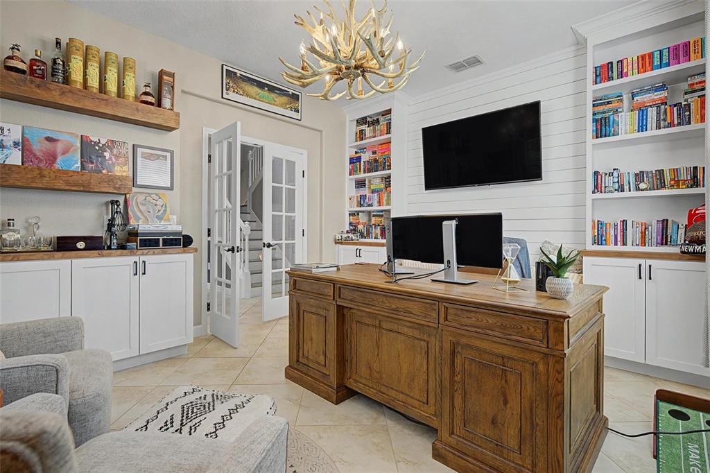 A home office features a wooden desk, built-in bookshelves, a television, and a chandelier — 3842 WELLINGBOROUGH COURT, LAND O LAKES, FL