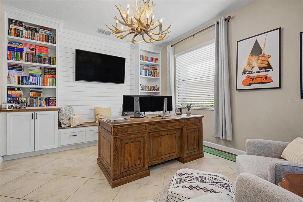 A home office features a wooden desk, built-in bookshelves, a television, and a chandelier — 3842 WELLINGBOROUGH COURT, LAND O LAKES, FL