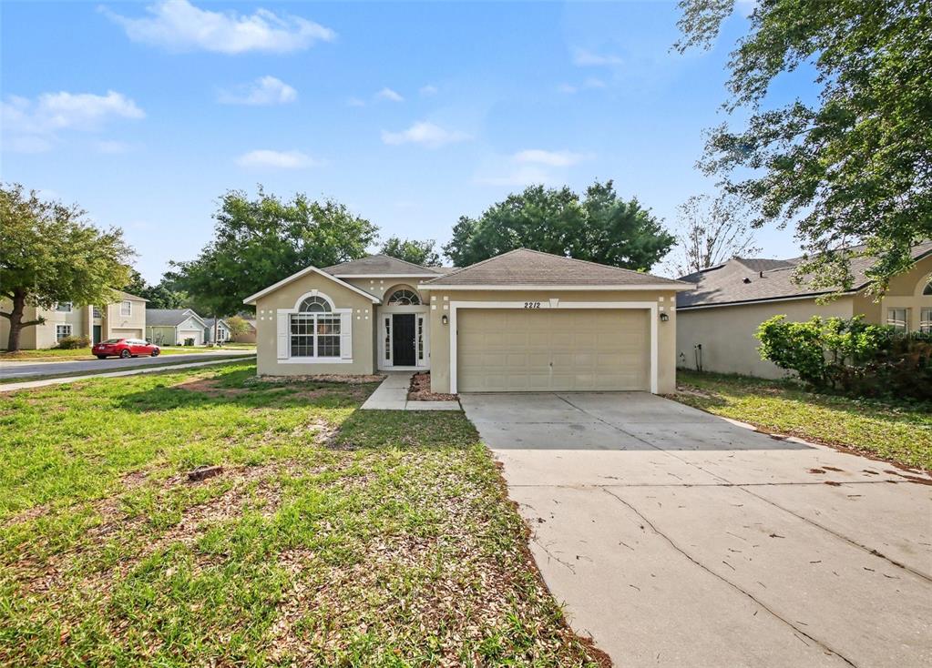 A single-story house with a beige exterior, a two-car garage, and a concrete driveway — 2212 NICOLLETT WAY, LEESBURG, FL