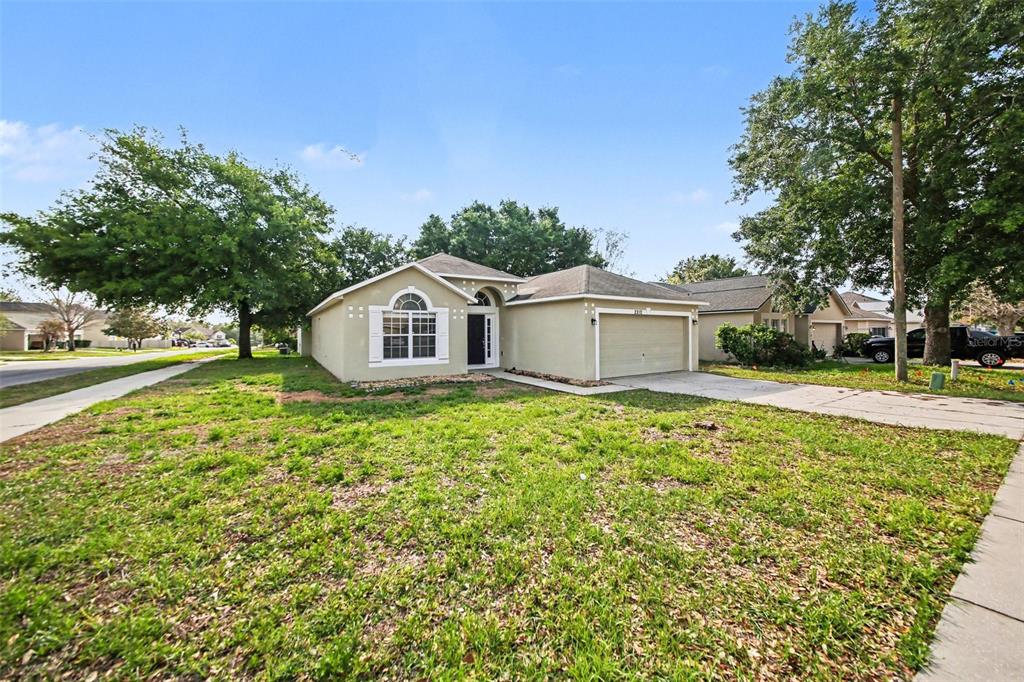 A single-story suburban house with a beige stucco exterior, a two-car garage, and a lawn — 2212 NICOLLETT WAY, LEESBURG, FL