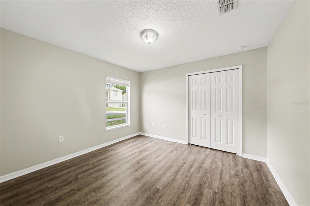 A bedroom with light gray walls, wood-look flooring, a single window, and white closet doors — 2212 NICOLLETT WAY, LEESBURG, FL