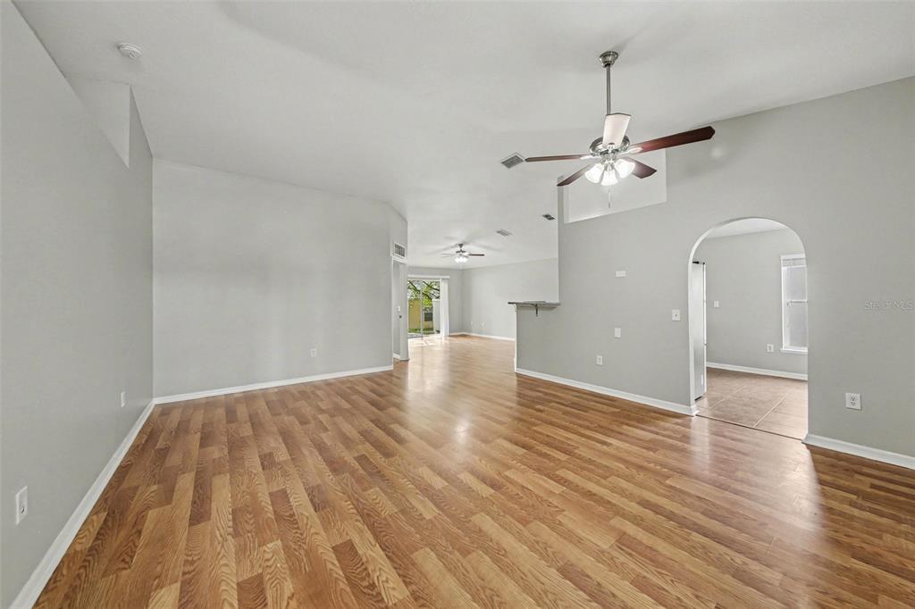 An empty living room with light gray walls, wood-look flooring, and a ceiling fan — 2212 NICOLLETT WAY, LEESBURG, FL