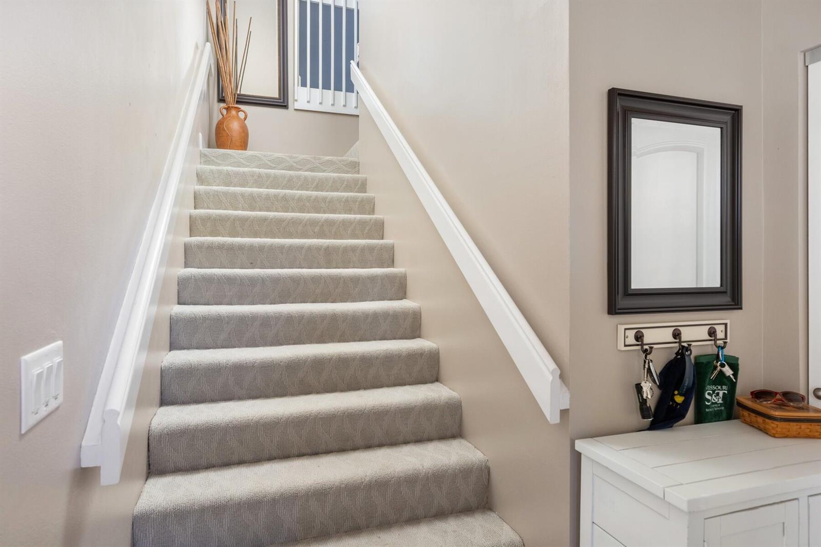 A carpeted staircase with white railings leads upward next to a wall with a mirror — VERO BEACH, FL