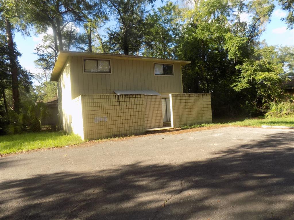 A two-story building with yellow vertical siding and a low-walled courtyard entrance — 713 SW 69 STREET, GAINESVILLE, FL