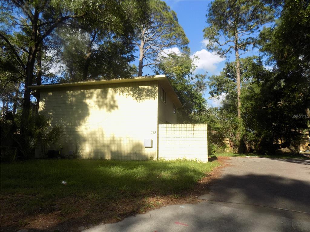 The exterior of a two-story yellow building with a concrete block wall and driveway — 713 SW 69 STREET, GAINESVILLE, FL
