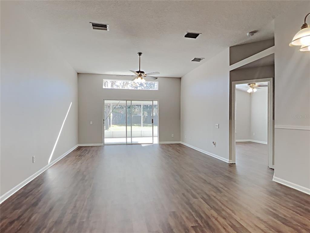 A spacious living room features wood-look flooring, a ceiling fan, and sliding glass patio doors — 12306 TWINKLING STAR PLACE, RIVERVIEW, FL