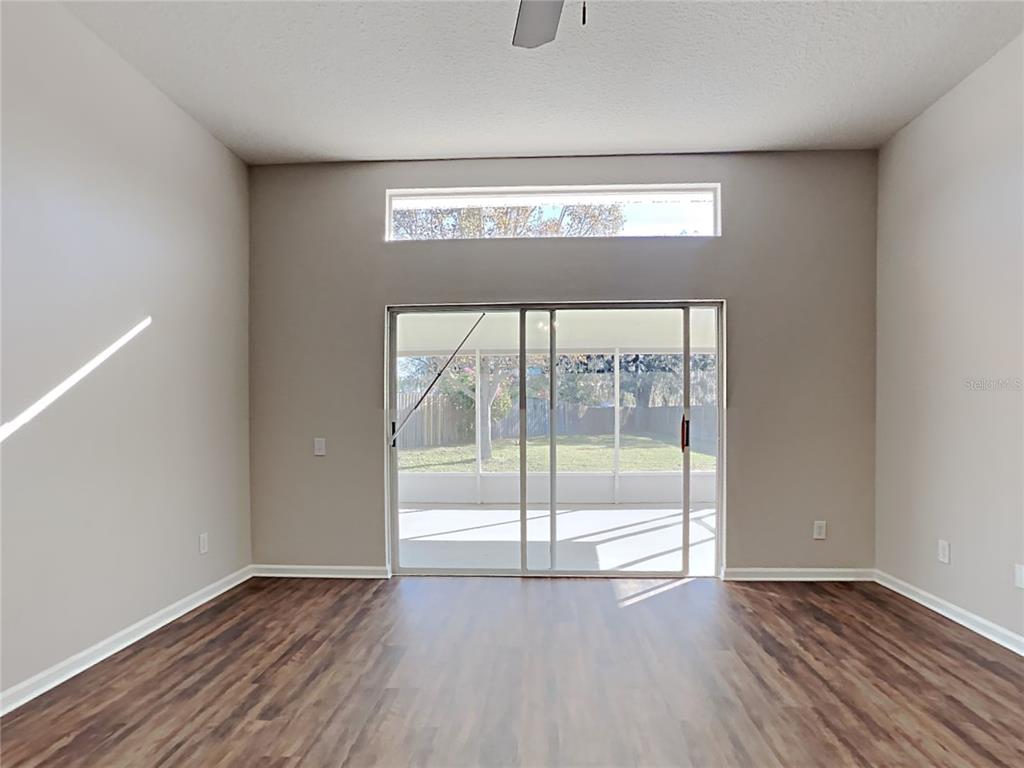 An empty room with wood-look flooring, a high ceiling, and sliding glass doors to a patio — 12306 TWINKLING STAR PLACE, RIVERVIEW, FL