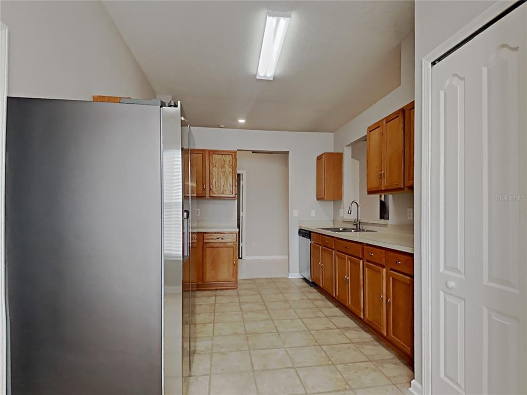 A kitchen features wood cabinets, light countertops, tile flooring, and a stainless steel refrigerator — 12306 TWINKLING STAR PLACE, RIVERVIEW, FL