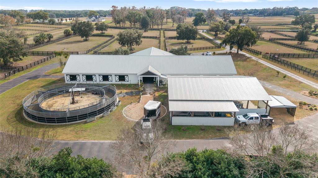An aerial view of a horse stable complex featuring a round pen and fenced pastures — 5575 NW 100TH STREET, OCALA, FL