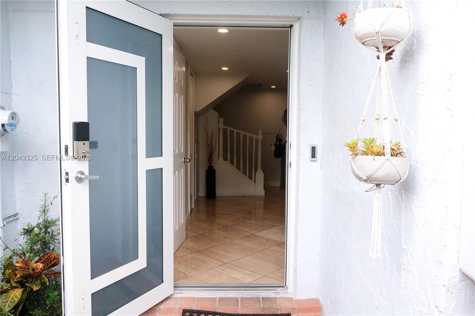 An open front door reveals a tiled entryway with a staircase and interior lighting — 400 NW 107th Ave # 10C, Miami FL 33172, MIAMI, FL