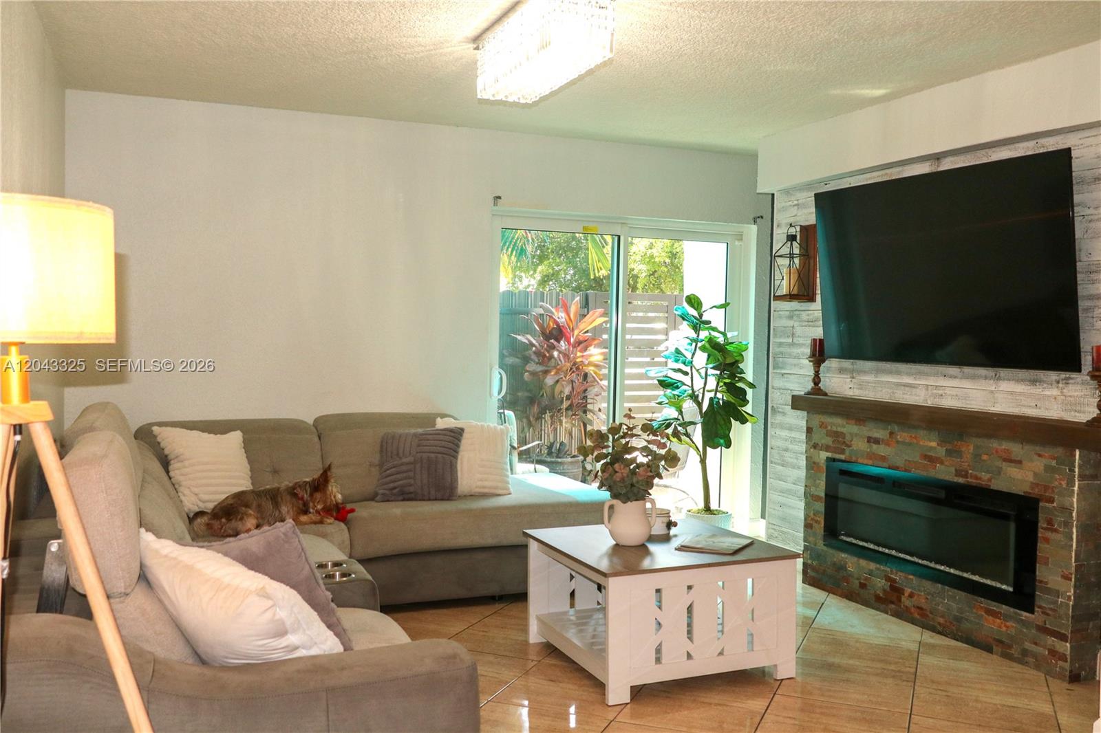 A living room features a sectional sofa, a fireplace with a television, and sliding doors — 400 NW 107th Ave # 10C, Miami FL 33172, MIAMI, FL