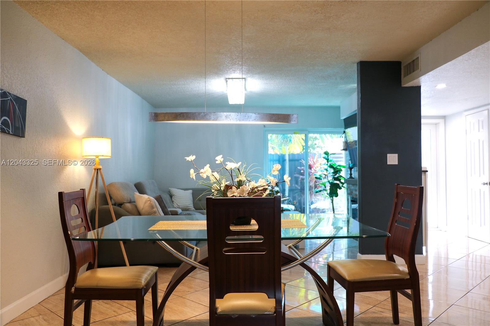 A dining area with a glass table and wooden chairs sits before a living room — 400 NW 107th Ave # 10C, Miami FL 33172, MIAMI, FL