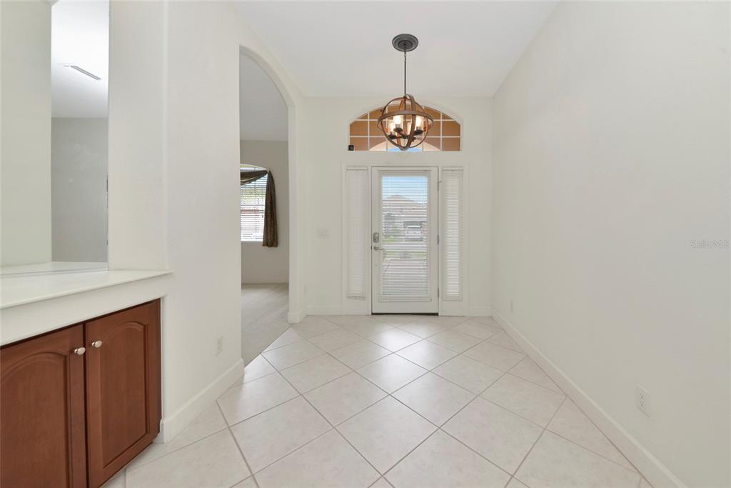 A bright entryway features tile flooring, a wooden chandelier, and a built-in wooden cabinet — 6841 74TH STREET CIRCLE E, BRADENTON, FL