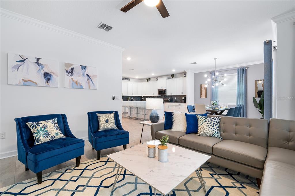 An open-concept living room features blue accent chairs, a gray sectional, and a modern kitchen — 3004 PROTAGONIST STREET, KISSIMMEE, FL