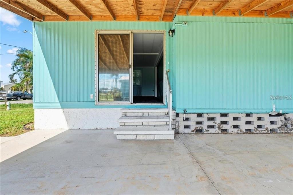 A turquoise mobile home exterior features a sliding glass door, concrete steps, and a carport — 8188 ROBERT STREET, ENGLEWOOD, FL