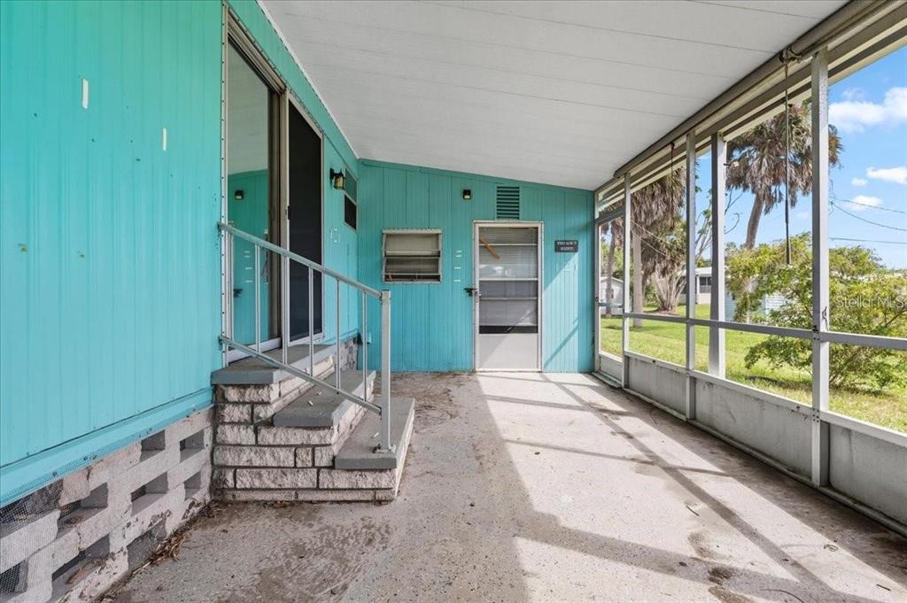 A covered screened-in porch with teal siding, concrete flooring, and steps leading to a door — 8188 ROBERT STREET, ENGLEWOOD, FL