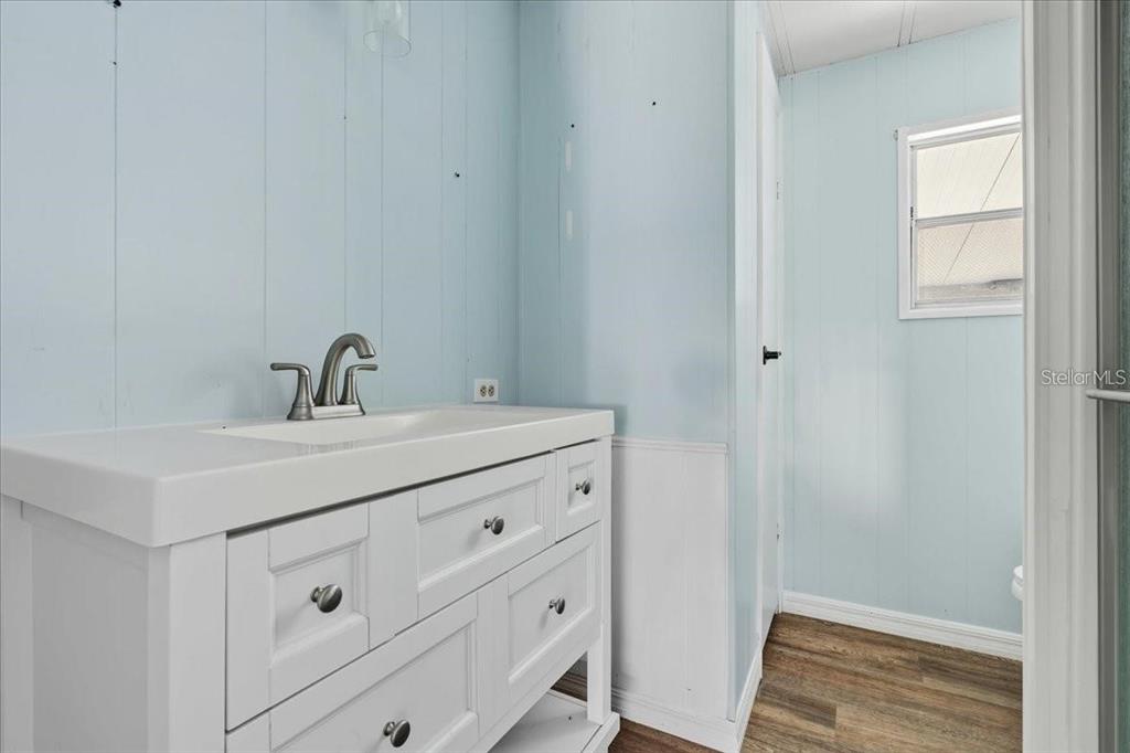 A bathroom features a white vanity with a sink, light blue walls, and wood flooring — 8188 ROBERT STREET, ENGLEWOOD, FL