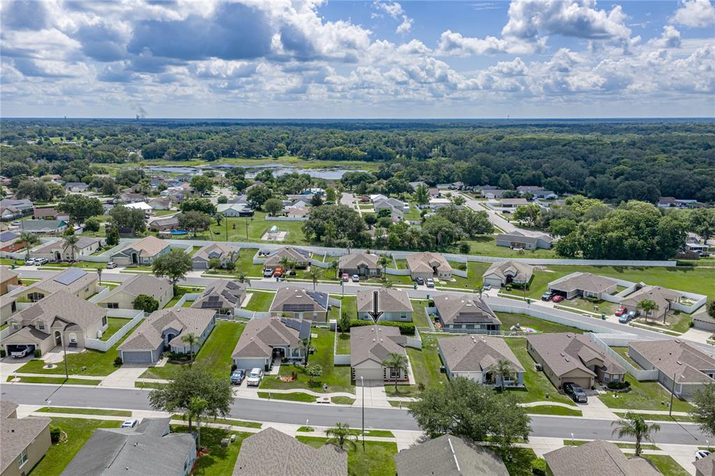 An aerial view shows a suburban neighborhood with single-family homes, lawns, and a distant lake — 7552 JENO STREET, ZEPHYRHILLS, FL