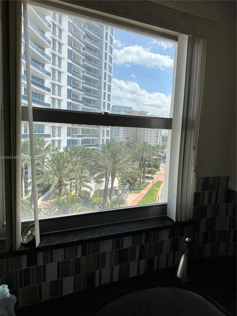 A kitchen window overlooks a street, palm trees, and a tall modern apartment building — 6039 Collins Ave # 728, Miami Beach FL 33140, MIAMI BEACH, FL