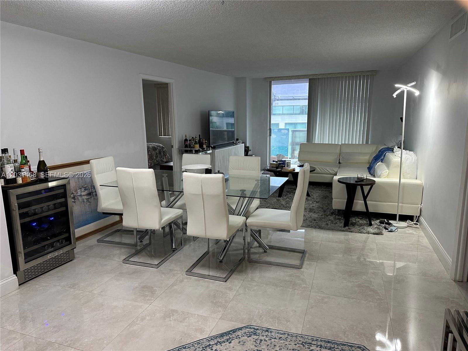 A dining area with a glass table and white chairs sits beside a living room — 6039 Collins Ave # 728, Miami Beach FL 33140, MIAMI BEACH, FL